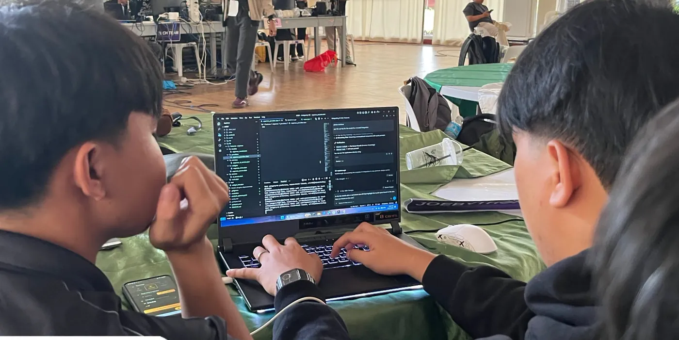 Two students building with an AI coding assistant on a laptop during the hackathon