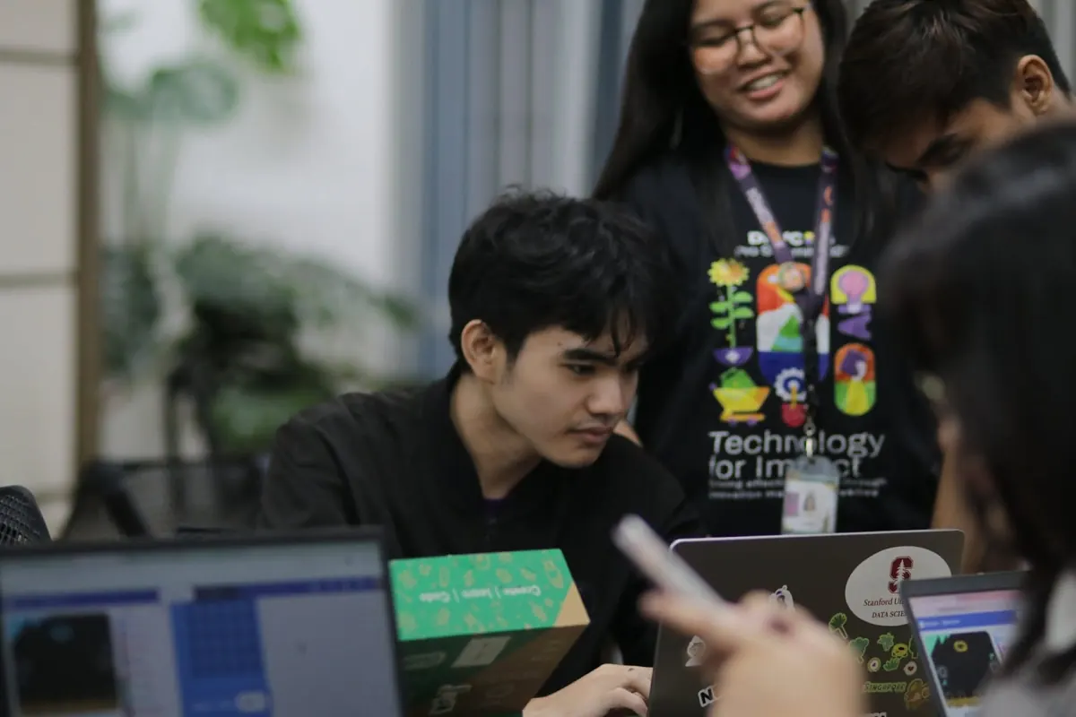 An intern concentrating on a laptop while a mentor looks on