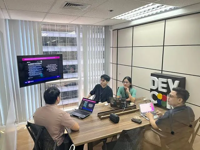 Interns and mentors reviewing speaker highlights in a meeting room with a DEVCON sign
